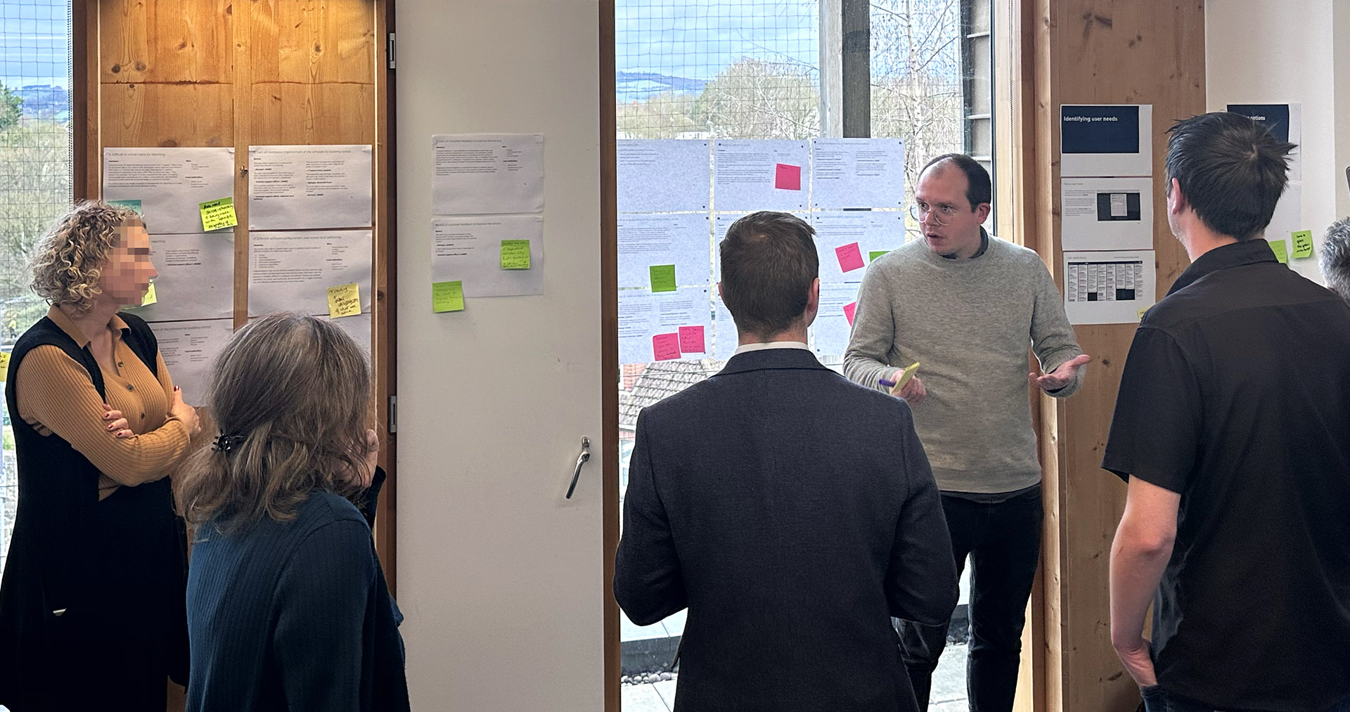 A group of people having a discussion in front of a window covered in paper and sticky notes